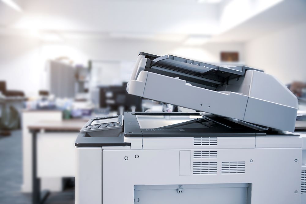 An office setting with a large multifunction printer in the foreground.