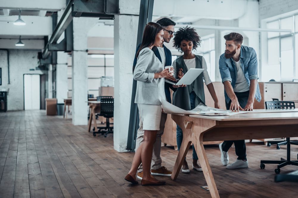 Group of young business people working together in creative office while standing near the wooden desk signifying Managed Print.